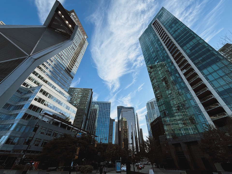 Glass towers rising above a city street beneath wispy clouds and a blue sky