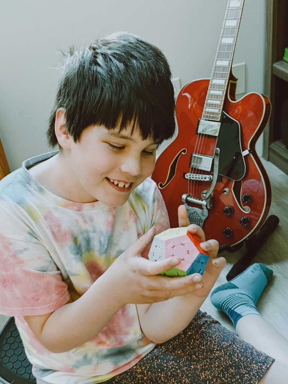 A smiling child holding a colourful puzzle beside a red guitar